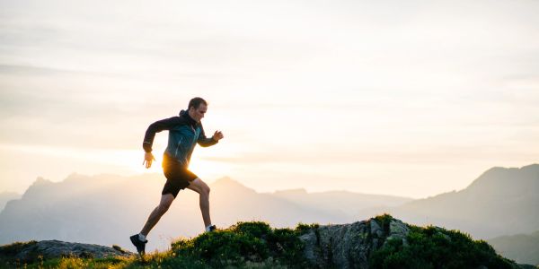 Man running on a mountain trail at sunrise.