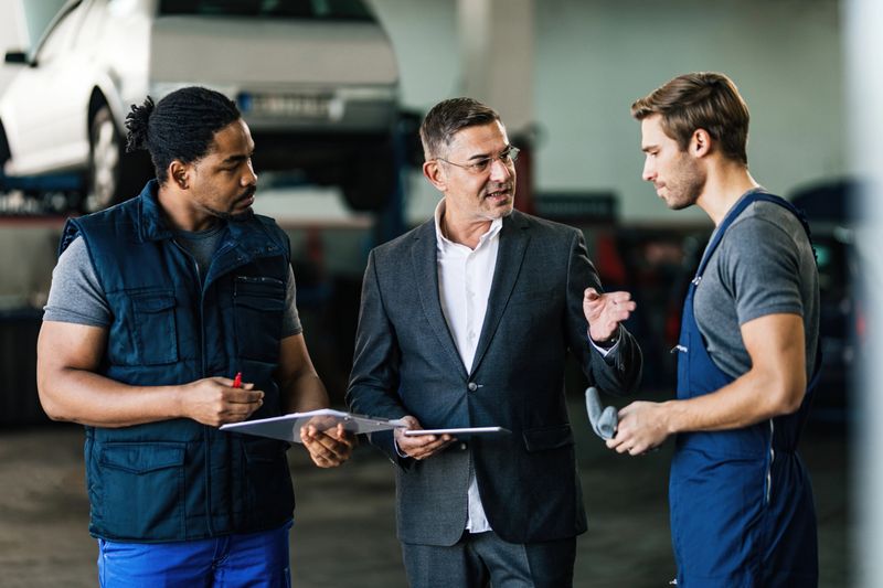 Young auto mechanics and manager communicating in a workshop. Focus is on manager.
