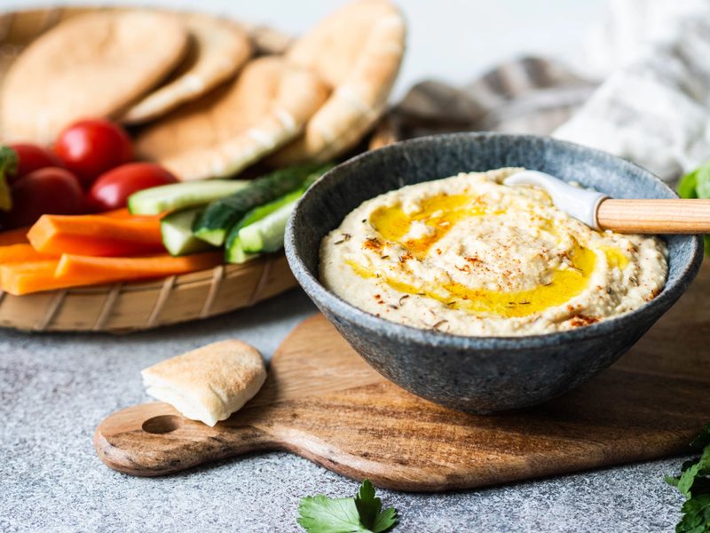 Homemade traditional spread hummus dip served with fresh vegetable , pita and herbs in tray on dark background. Copy space