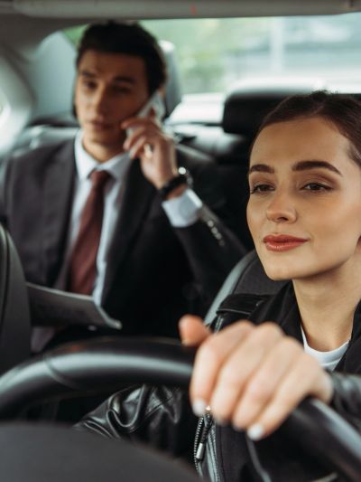 Woman driving a car, man using phone in backseat.