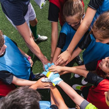 Children joining hands in a team huddle during sports.