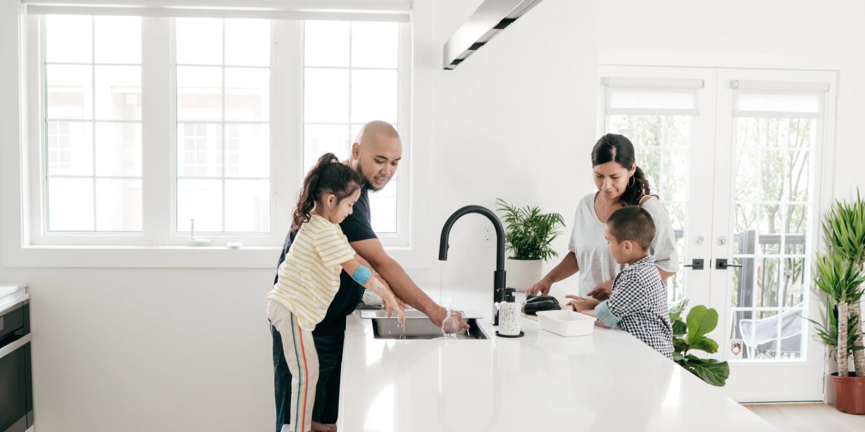 Family washing hands together in a bright, modern kitchen.
