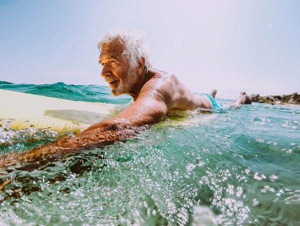 A smiling Mentawai Surfer is paddling on his surfboard in the ocean.