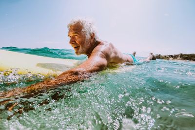 A smiling Mentawai Surfer paddling on his surfboard in the ocean.