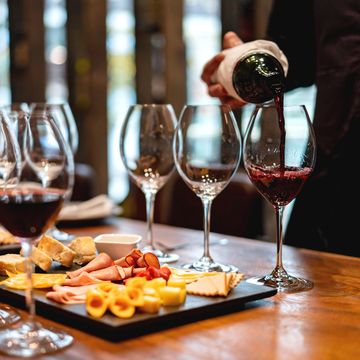 Wine being poured alongside cheese and charcuterie on a wooden table.