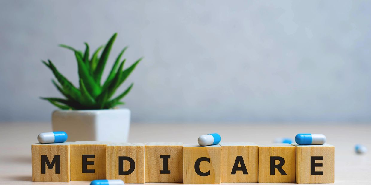 Wooden blocks spell Medicare with capsules and a small plant in the background.
