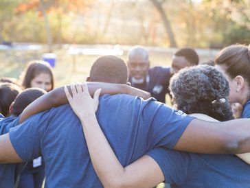 A group of people in a close huddle outdoors, showing unity and support.