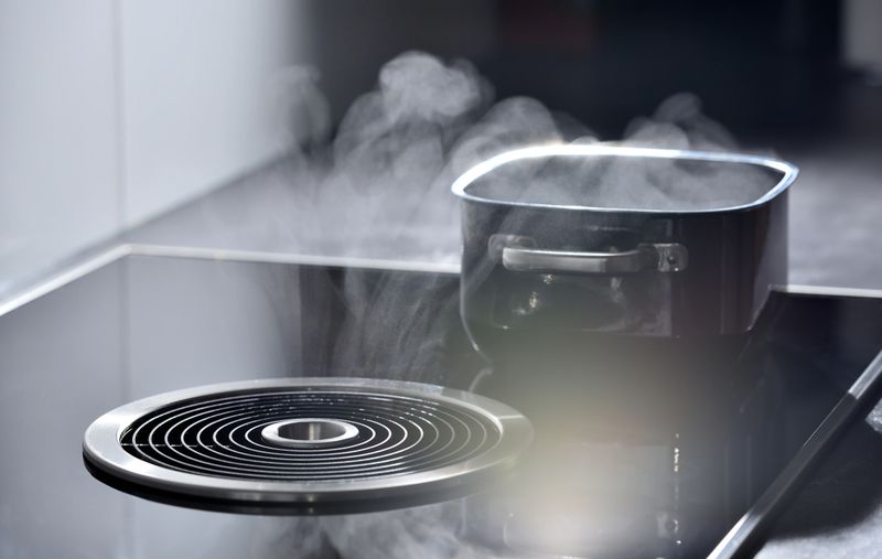 Electric induction cooker with built-in ventilation and extractor hood which draws steam from boiling water in a pan