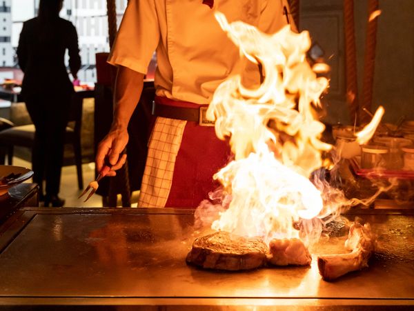 Chef flambéing meat on a grill with dramatic flames.