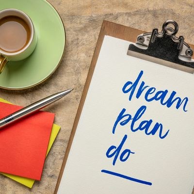 Clipboard with 'dream plan do' written, next to a cup of coffee and colorful notes.