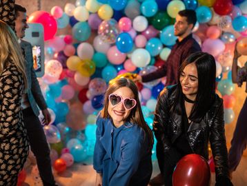 Young people enjoying a colorful balloon party with heart-shaped sunglasses.