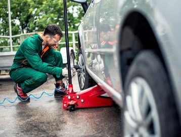 Mechanic in green overalls inflating a car tire outdoors using an air compressor.
