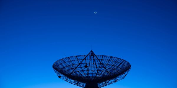 Antena parabólica al atardecer con luna creciente.
