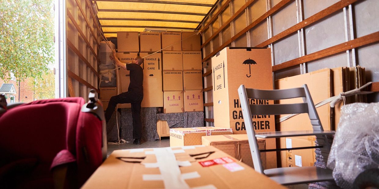 A person organizing boxes inside a moving truck filled with packed items.