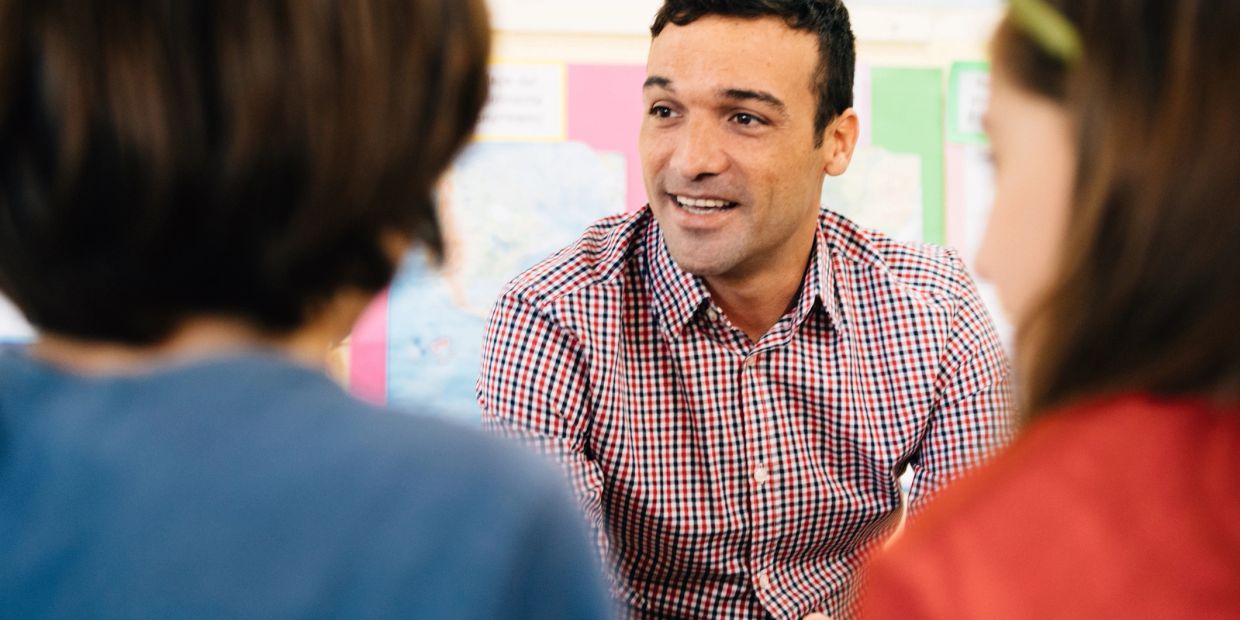 Man in checkered shirt talking to two people in a classroom.