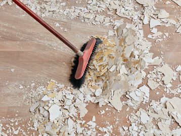 A broom sweeping up paint chips and dust from a wooden floor.