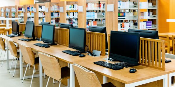 Library computer station with wooden desks and shelves full of books.