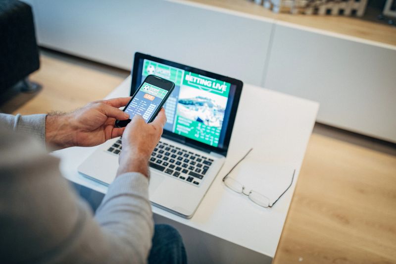 Mature man using mobile app for live betting and online gambling and watching a sports match