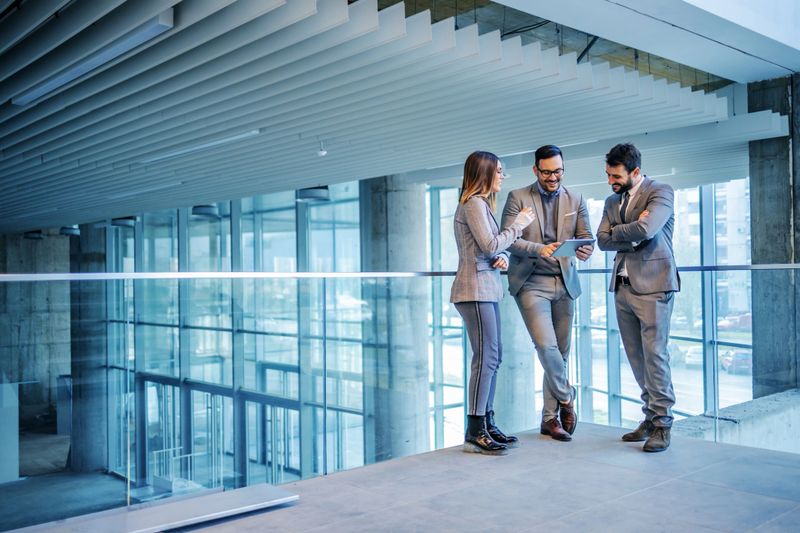 Group of successful real estate agents standing in building in construction process and looking at tablet. Man in the middle showing to his colleagues price on the market for that building.