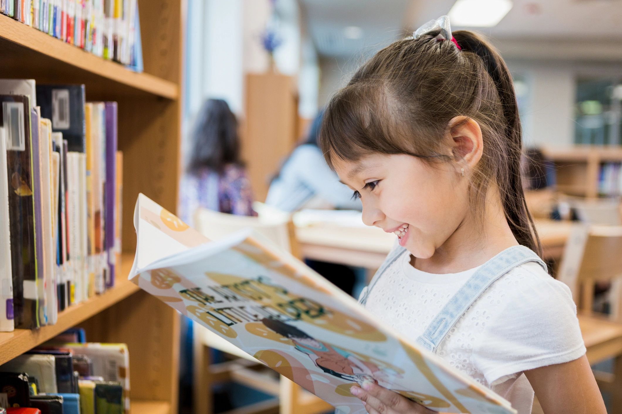 A girl happily reading a book in a library.