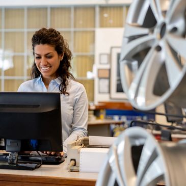 Smiling woman working on a computer in a car dealership showroom.