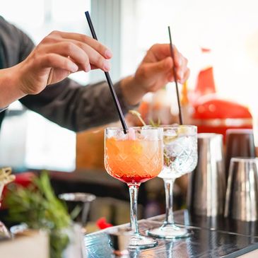 Bartender stirring cocktails with straws at a bar.