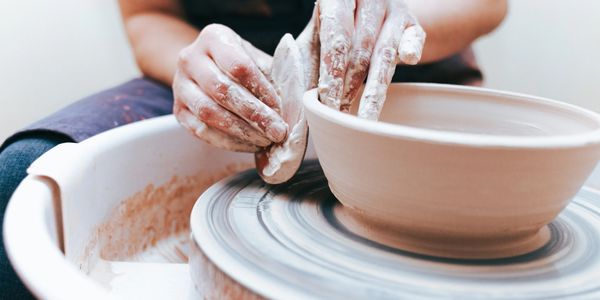 Hands shaping clay on a pottery wheel creating a bowl.