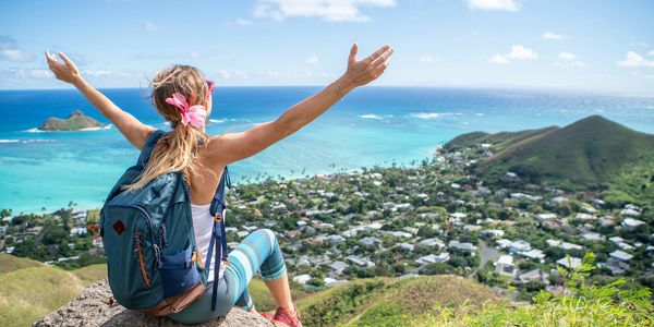 Woman with backpack enjoys scenic ocean view from a hilltop.