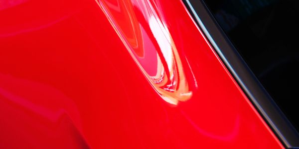 Close-up of a shiny red car body near the window.