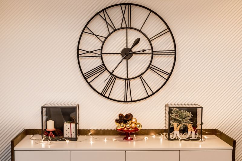 Christmas decoration with glass ornaments and lights. Big metal modern wall clock on the white striped wall.