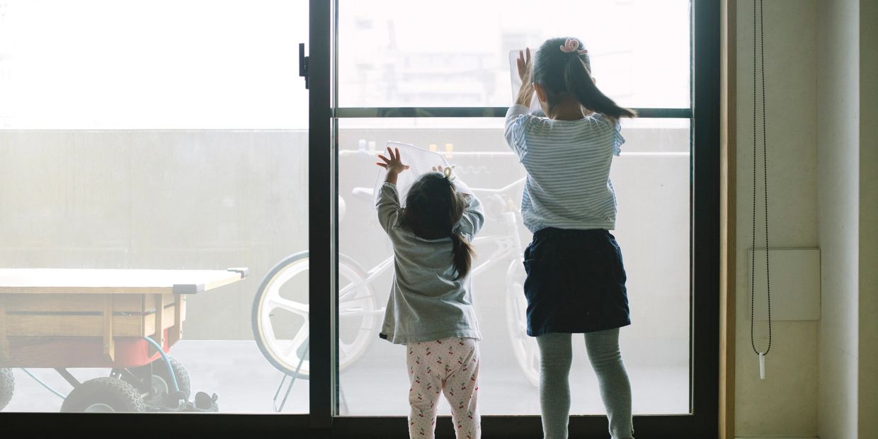 Two young children reaching up to a large glass door inside a bright room.