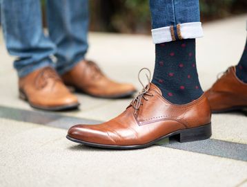 Brown leather dress shoes worn with rolled-up jeans and polka dot socks.