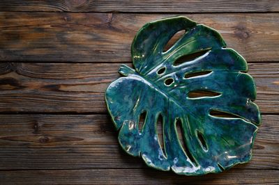 A glossy ceramic plate shaped like a green monstera leaf on wooden surface.