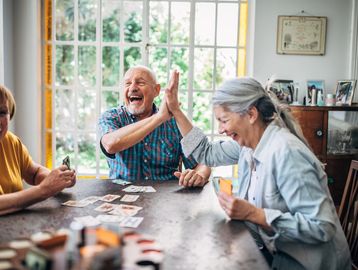 Seniors joyfully playing a card game and high-fiving.