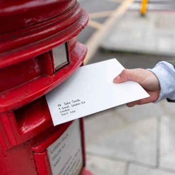 Person posting a letter into a traditional red mailbox.
