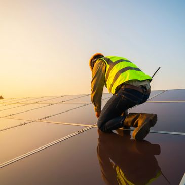 Worker installing solar panels at sunset, wearing safety gear.