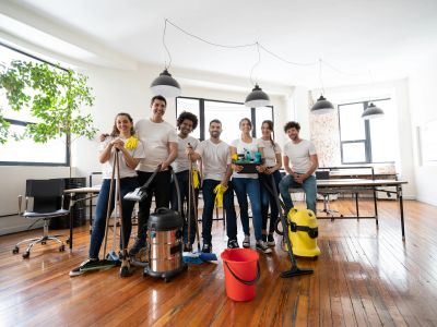 A group of young people posing with cleaning equipment in a bright room.