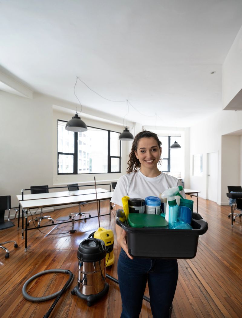 Portrait of young female cleaner at an office holding cleaning supplies smiling at camera very cheerfully
