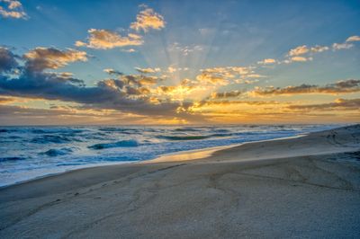 Sunset over a sandy beach with waves and dramatic clouds.