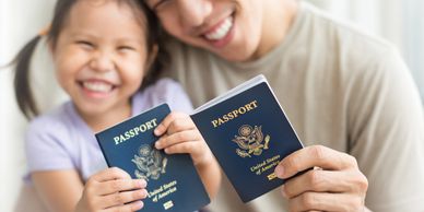 A parent and child smiling and holding passports to the camera.