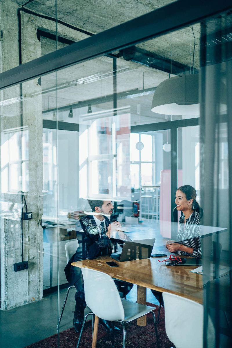 Shot of two young business persons on meeting in the conference room. The view is through glass wall.