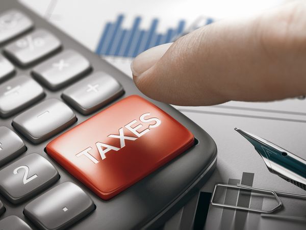 Finger pressing a red 'TAXES' button on a calculator with documents and pen nearby.