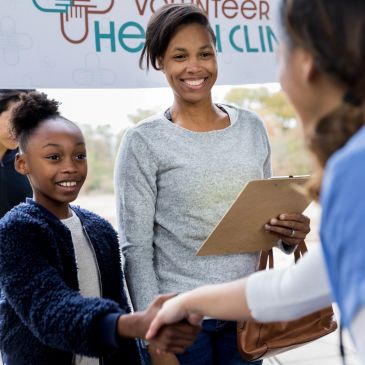 Smiling woman and girl at volunteer health clinic shaking hands.