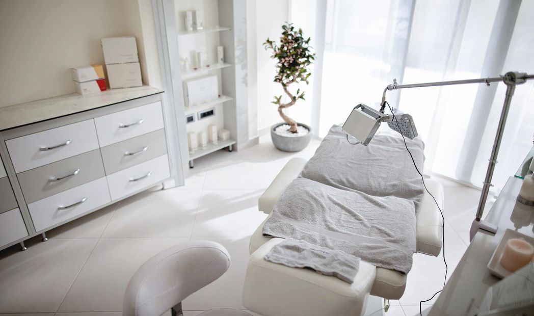 Bright, clean spa treatment room with white furniture and gray towels.