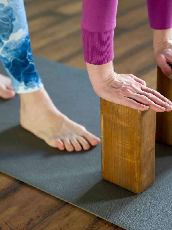 Person using wooden blocks for support during yoga on a mat.