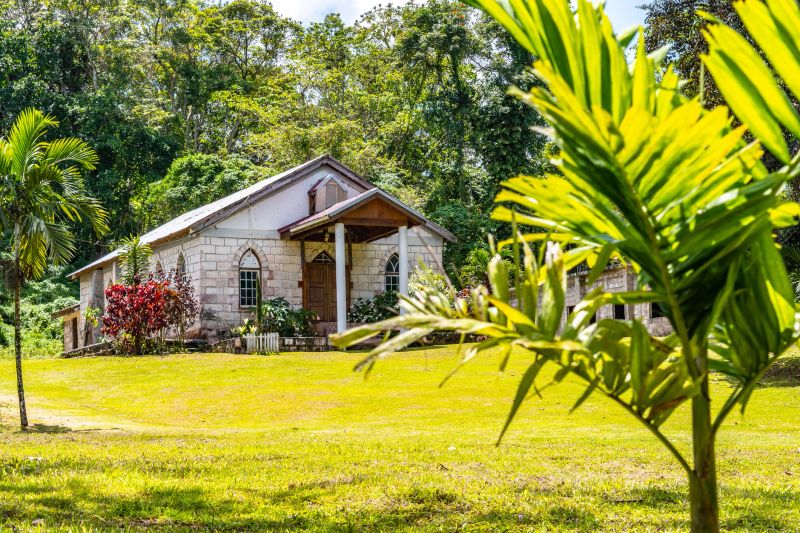 Small modest old brick wall chapel, built in 1903, in a Caribbean island countryside. All Saints Anglican Church in Chester Castle town, Hanover parish, Jamaica, surrounded by lush green landscape.