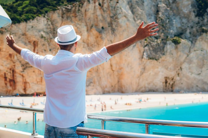 Young caucasian elegant man enjoying his vacation. Standing on boat with outstretched arms.