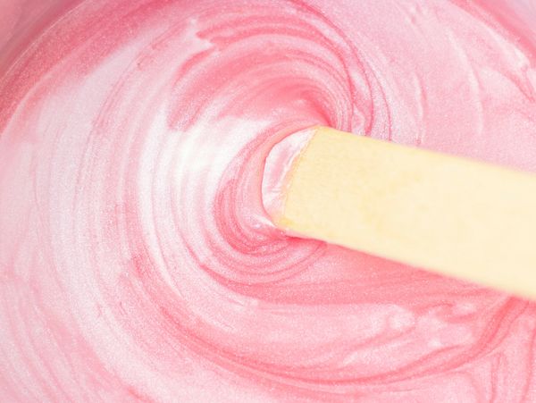Close-up of a wooden stick stirring shiny pink cream or frosting.