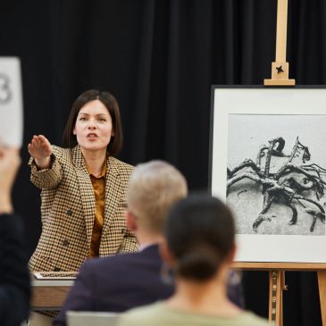 Woman auctioneer bidding in front of audience with crab photo.