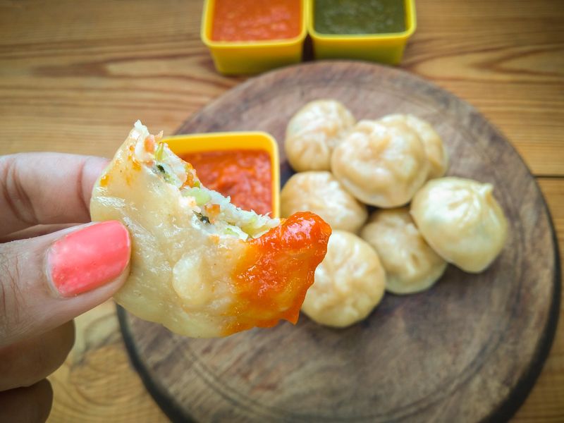 Close-up of hand dipping momos (dumpling) in red chutney (sauce).